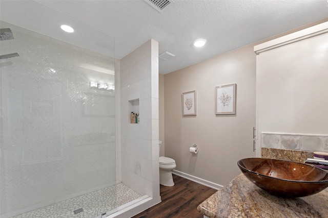 bathroom with a tile shower, vanity, a textured ceiling, hardwood / wood-style flooring, and toilet