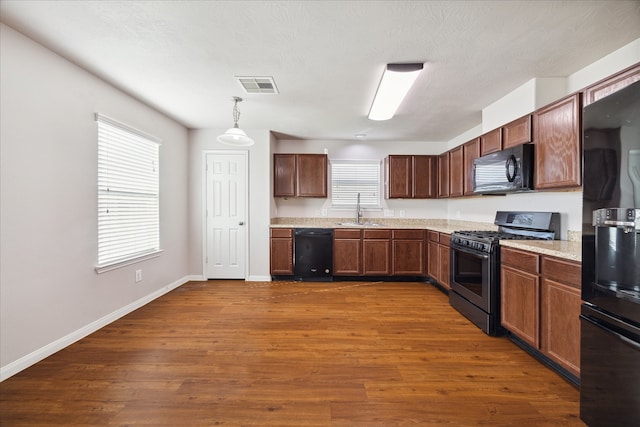 kitchen featuring dark wood-type flooring, hanging light fixtures, black appliances, and sink