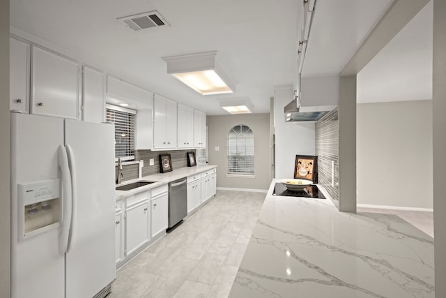 kitchen with light stone countertops, stainless steel dishwasher, sink, white cabinets, and white fridge with ice dispenser