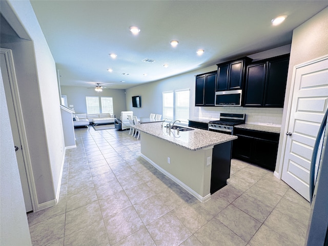 kitchen featuring ceiling fan, sink, stainless steel appliances, tasteful backsplash, and an island with sink