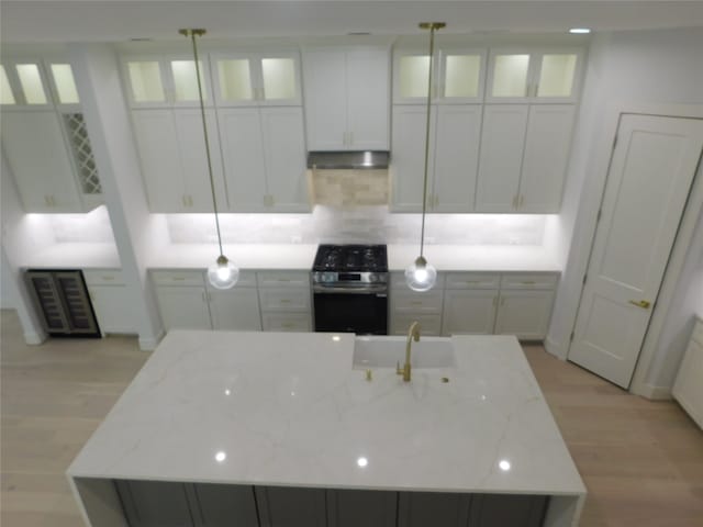 kitchen with a center island with sink, decorative light fixtures, light stone counters, and stainless steel range with electric cooktop