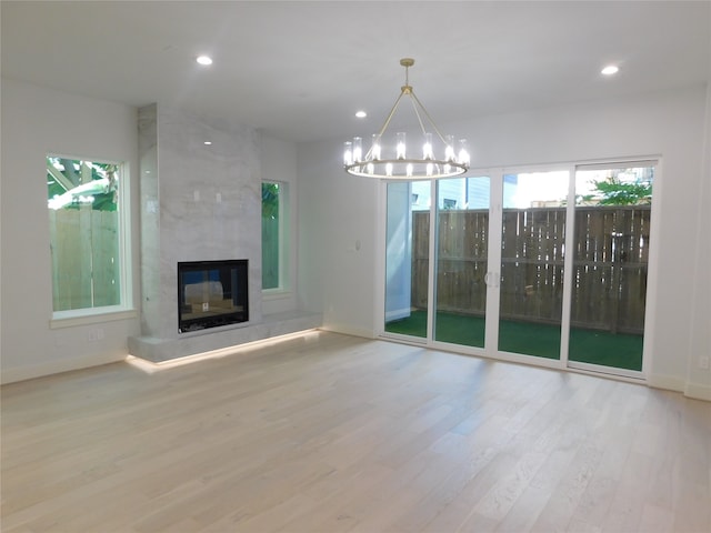 unfurnished living room with a large fireplace, light hardwood / wood-style floors, and a notable chandelier