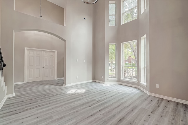 unfurnished living room with light wood-type flooring and a towering ceiling