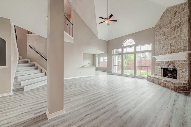 unfurnished living room with a fireplace, light wood-type flooring, high vaulted ceiling, and ceiling fan