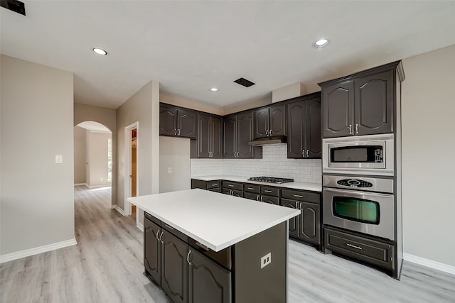 kitchen with a center island, stainless steel appliances, decorative backsplash, dark brown cabinets, and light wood-type flooring