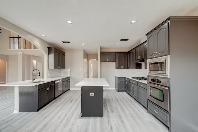 kitchen featuring appliances with stainless steel finishes, backsplash, sink, light hardwood / wood-style flooring, and a center island