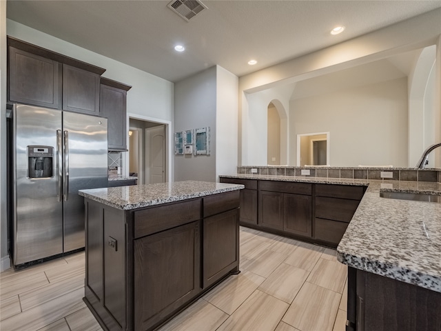 kitchen featuring stainless steel fridge with ice dispenser, sink, a kitchen island, and light stone counters