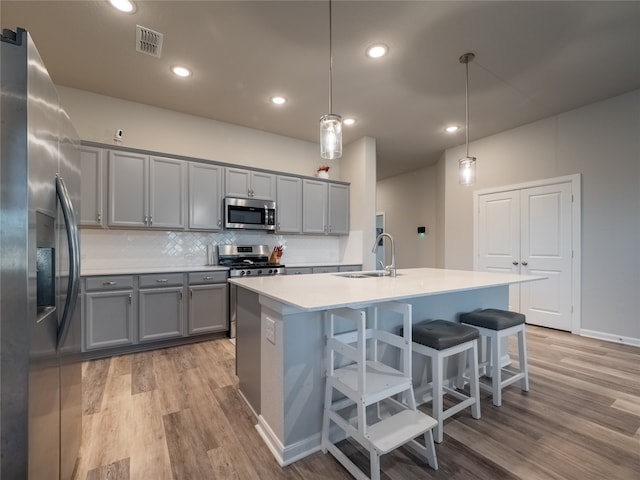 kitchen with hanging light fixtures, stainless steel appliances, tasteful backsplash, light hardwood / wood-style flooring, and a kitchen island with sink