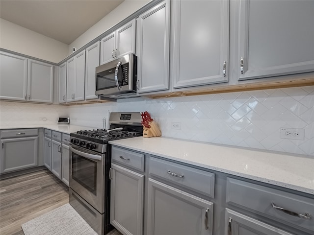 kitchen with decorative backsplash, light hardwood / wood-style flooring, light stone countertops, and appliances with stainless steel finishes