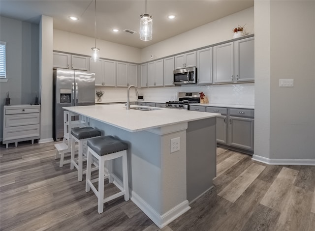 kitchen with sink, hanging light fixtures, gray cabinets, an island with sink, and stainless steel appliances