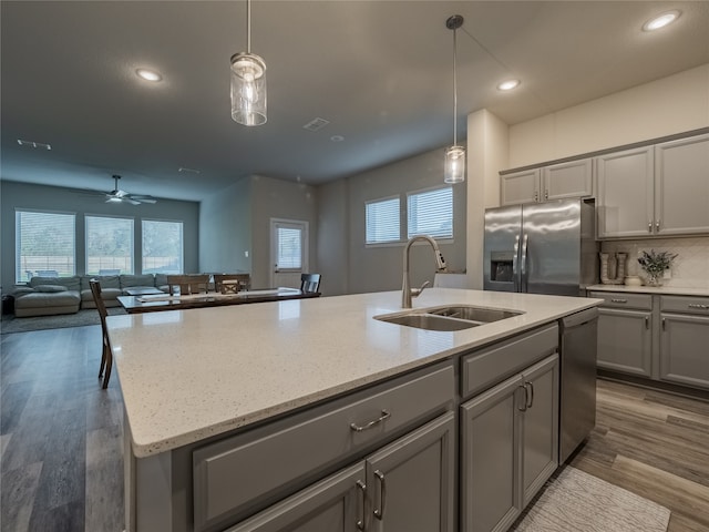 kitchen featuring sink, stainless steel appliances, pendant lighting, a center island with sink, and hardwood / wood-style flooring