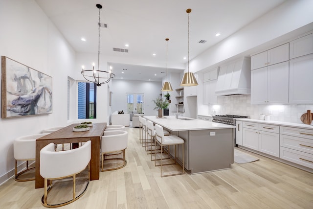 kitchen with white cabinetry, a kitchen breakfast bar, an island with sink, decorative light fixtures, and custom exhaust hood