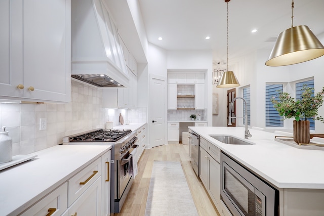 kitchen with sink, white cabinetry, appliances with stainless steel finishes, custom range hood, and pendant lighting