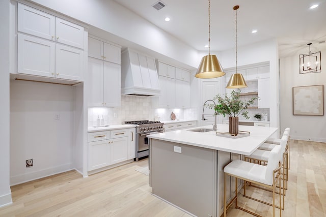 kitchen with sink, white cabinetry, hanging light fixtures, high end stainless steel range, and custom exhaust hood