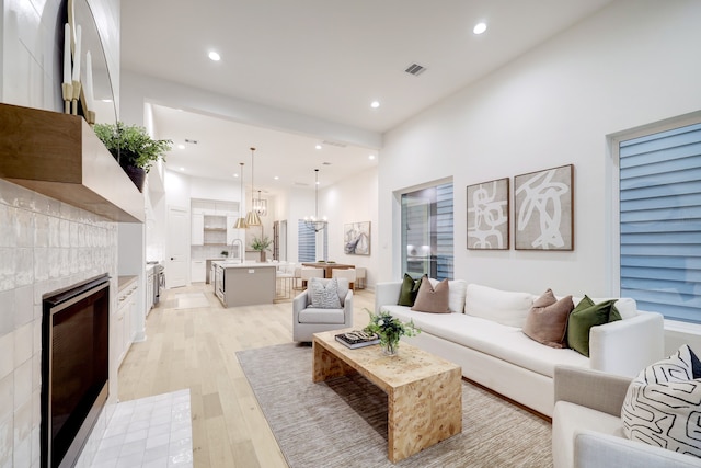 living room with a tiled fireplace, sink, a notable chandelier, and light hardwood / wood-style flooring