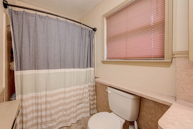 bathroom with toilet, a textured ceiling, and tile walls