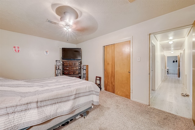 bedroom with a closet, a textured ceiling, light colored carpet, and ceiling fan