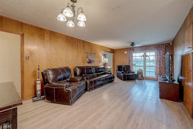 living room with ceiling fan with notable chandelier, light hardwood / wood-style floors, a textured ceiling, and wooden walls