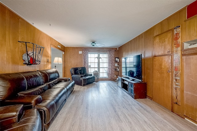 living room with ceiling fan, wood walls, light wood-type flooring, and a textured ceiling