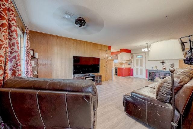 living room with a notable chandelier, light wood-type flooring, and wooden walls