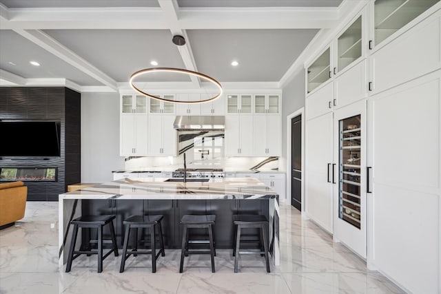 kitchen with beam ceiling, light stone counters, a center island with sink, and white cabinets