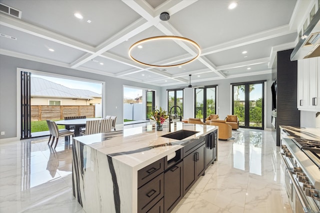 kitchen with light stone countertops, french doors, sink, a center island with sink, and double oven range