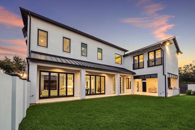 back house at dusk featuring a lawn