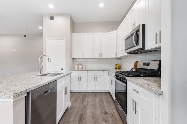 kitchen with sink, backsplash, light hardwood / wood-style floors, white cabinets, and appliances with stainless steel finishes