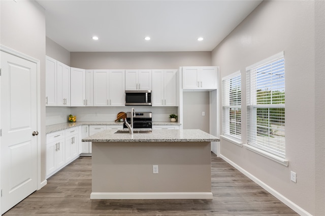 kitchen featuring light stone counters, stainless steel appliances, a kitchen island with sink, sink, and white cabinetry