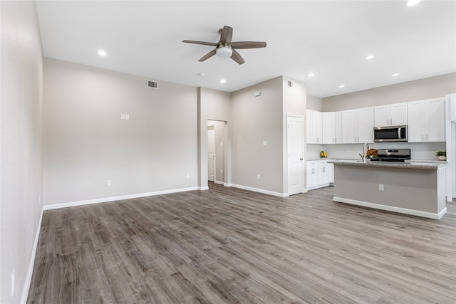 kitchen featuring white cabinets, light hardwood / wood-style flooring, light stone countertops, an island with sink, and stainless steel appliances