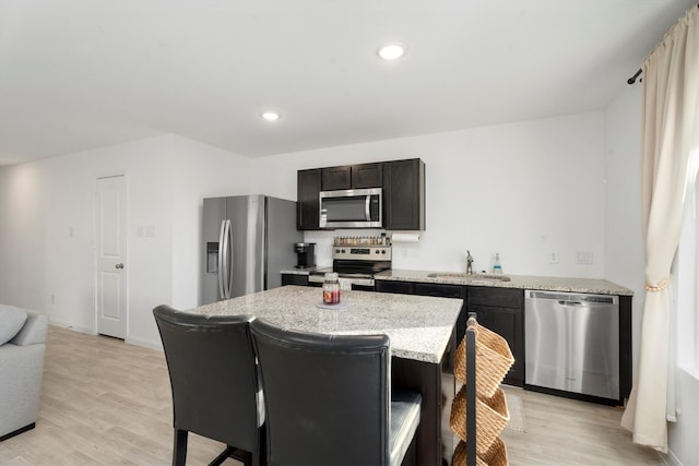 kitchen with a center island, sink, light hardwood / wood-style flooring, light stone countertops, and stainless steel appliances