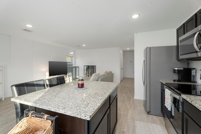 kitchen with light stone countertops, a center island, stainless steel appliances, a kitchen bar, and light wood-type flooring