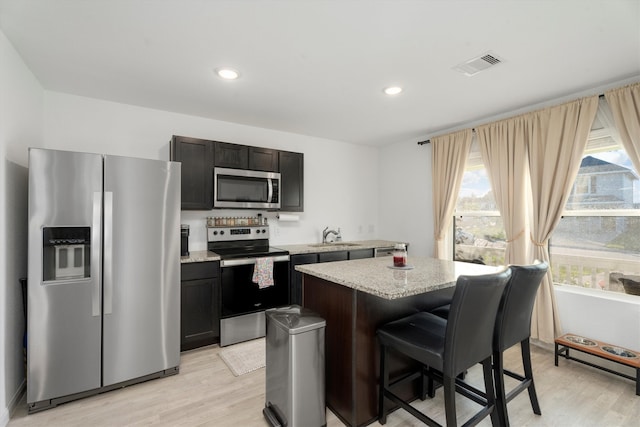 kitchen with appliances with stainless steel finishes, dark brown cabinets, sink, a center island, and light hardwood / wood-style floors