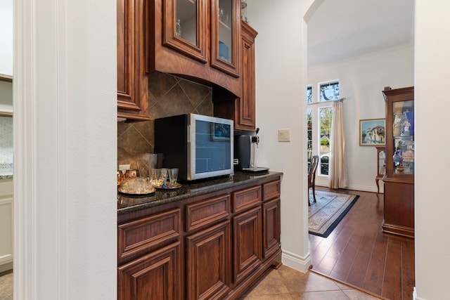 kitchen with tasteful backsplash, dark stone counters, wood-type flooring, and ornamental molding