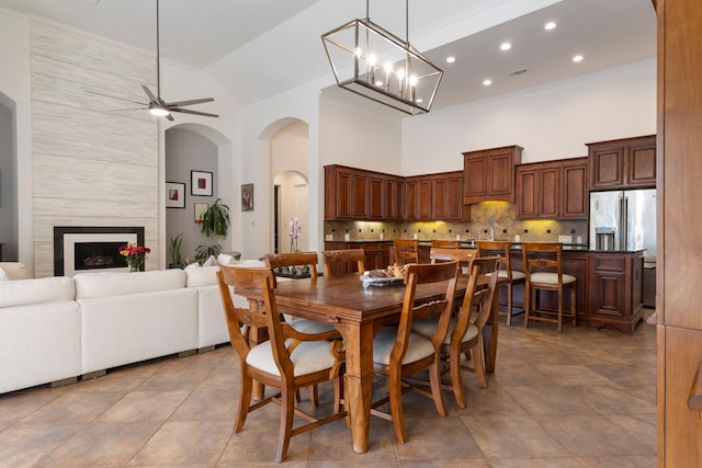 dining room with a fireplace, light tile patterned floors, ceiling fan with notable chandelier, and high vaulted ceiling