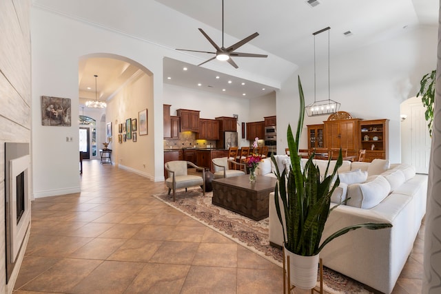 living room featuring light tile patterned floors, high vaulted ceiling, ceiling fan with notable chandelier, and ornamental molding