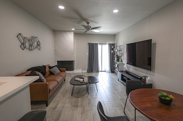 living room with a fireplace, ceiling fan, light hardwood / wood-style flooring, and a textured ceiling