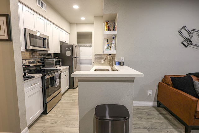 kitchen featuring white cabinets, kitchen peninsula, stainless steel appliances, and tasteful backsplash