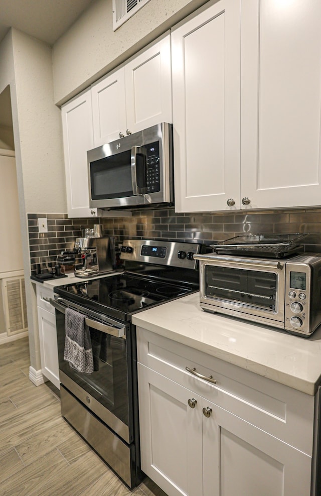 kitchen with backsplash, light stone counters, white cabinets, and appliances with stainless steel finishes