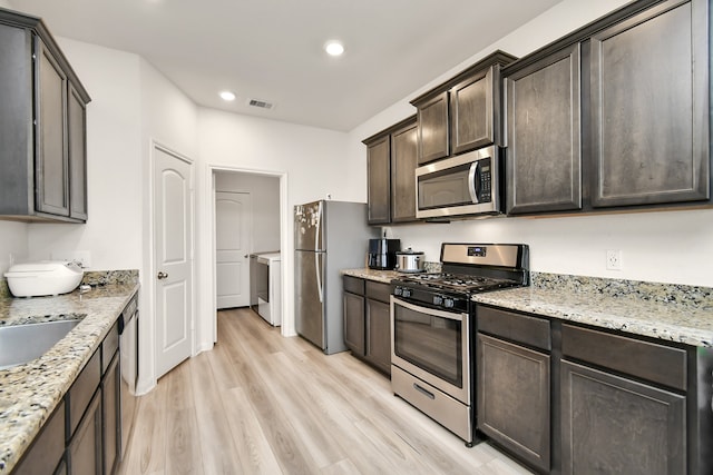 kitchen featuring light stone counters, washer / dryer, dark brown cabinets, appliances with stainless steel finishes, and light wood-type flooring