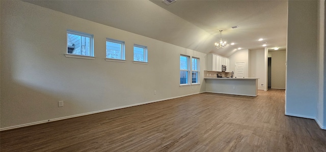 unfurnished living room with an inviting chandelier, wood-type flooring, sink, and vaulted ceiling