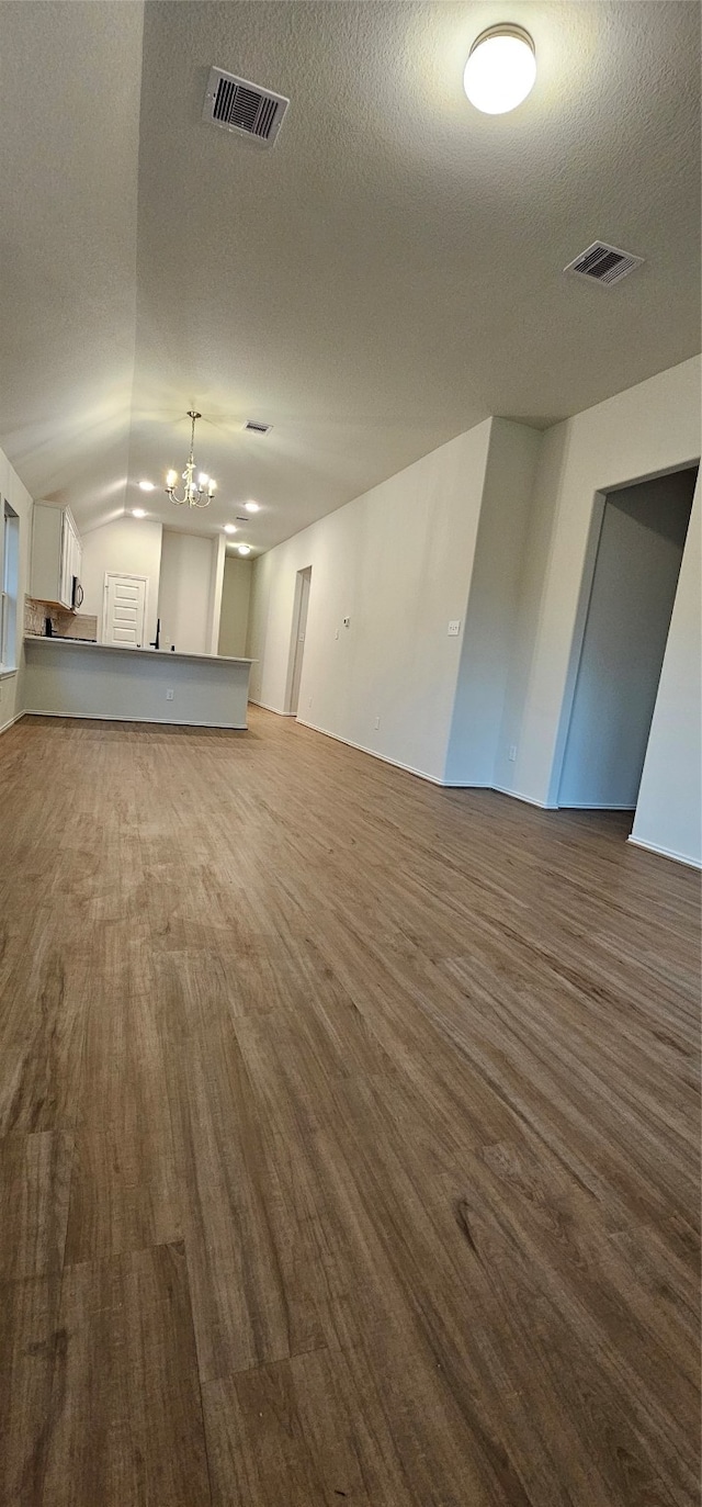 unfurnished living room featuring a textured ceiling, wood-type flooring, vaulted ceiling, and a notable chandelier