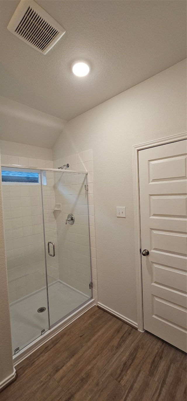 bathroom featuring a textured ceiling, hardwood / wood-style flooring, a shower with door, and lofted ceiling