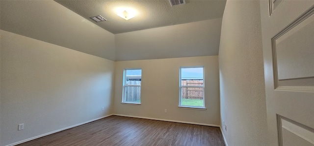 spare room featuring a textured ceiling, dark wood-type flooring, and vaulted ceiling