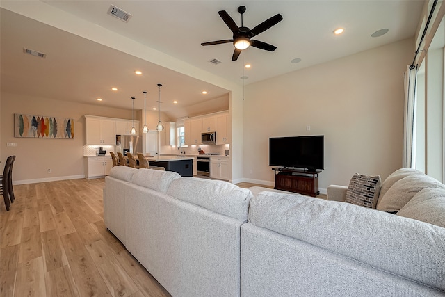 living room with light wood-type flooring, ceiling fan, and sink