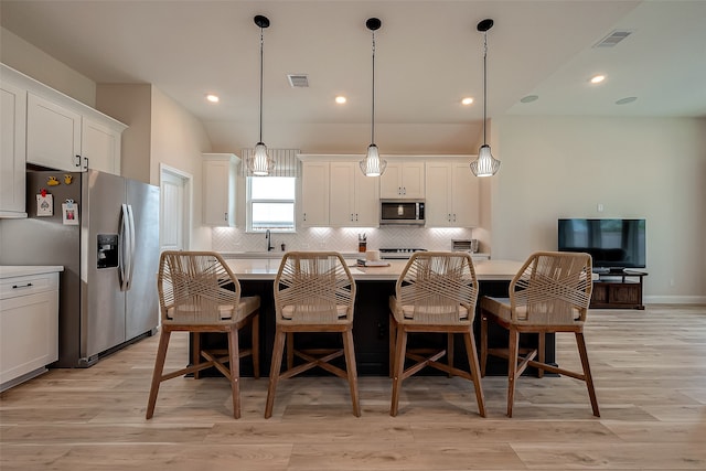 kitchen featuring white cabinets, decorative light fixtures, stainless steel appliances, and light hardwood / wood-style flooring