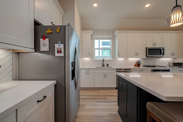 kitchen with light wood-type flooring, stainless steel appliances, sink, pendant lighting, and white cabinetry