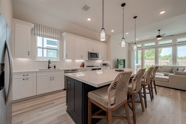 kitchen featuring appliances with stainless steel finishes, light wood-type flooring, decorative light fixtures, white cabinets, and a kitchen island