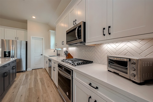 kitchen with sink, appliances with stainless steel finishes, decorative backsplash, white cabinets, and light wood-type flooring