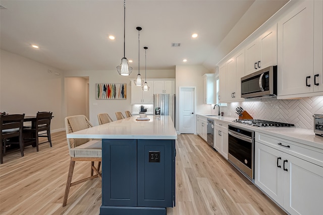 kitchen featuring light hardwood / wood-style floors, pendant lighting, a kitchen bar, a kitchen island, and appliances with stainless steel finishes